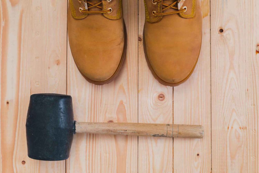 Nubuck schoenen met lichte vlekken naast een rubberen hamer op houten vloer