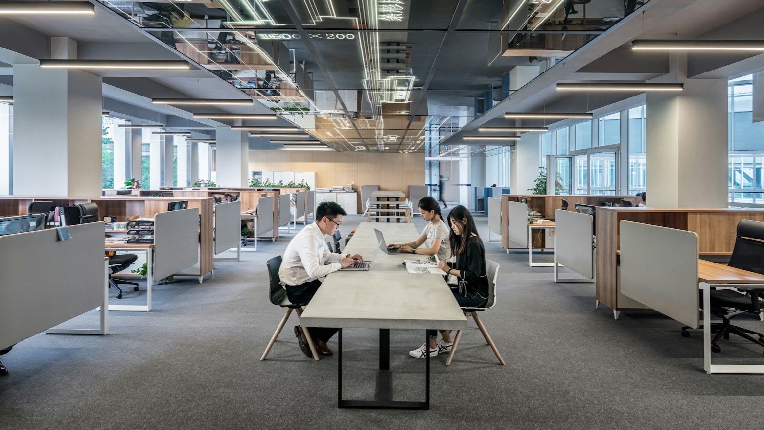 Moderne kantoorruimte met drie collega&rsquo;s die samenwerken aan een lange tafel, passend bij een cadeau voor collega&rsquo;s