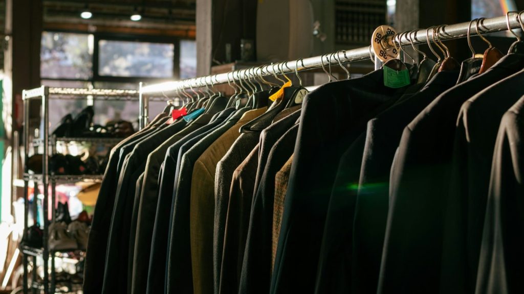 Tweedehands kledingrekken met diverse donkere jassen in een winkel met natuurlijk licht