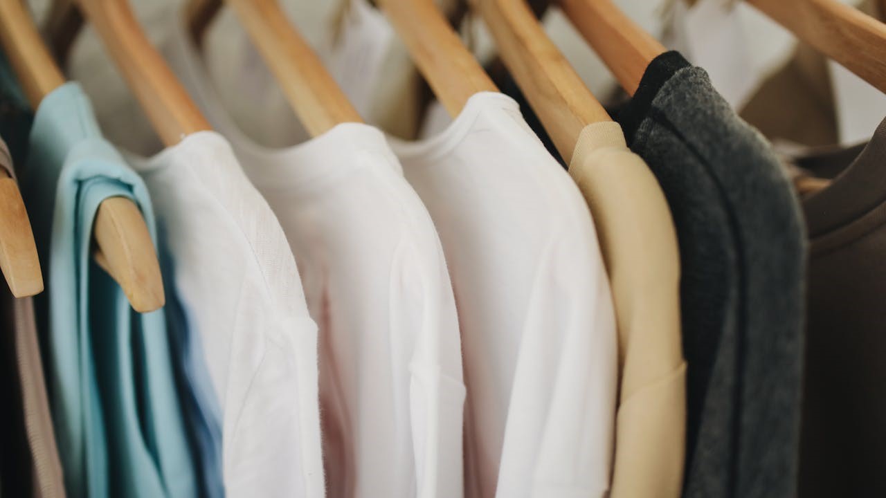 Kleding sorteren op houten hangers in een overzichtelijke kledingkast, met witte en gekleurde shirts op een rij.