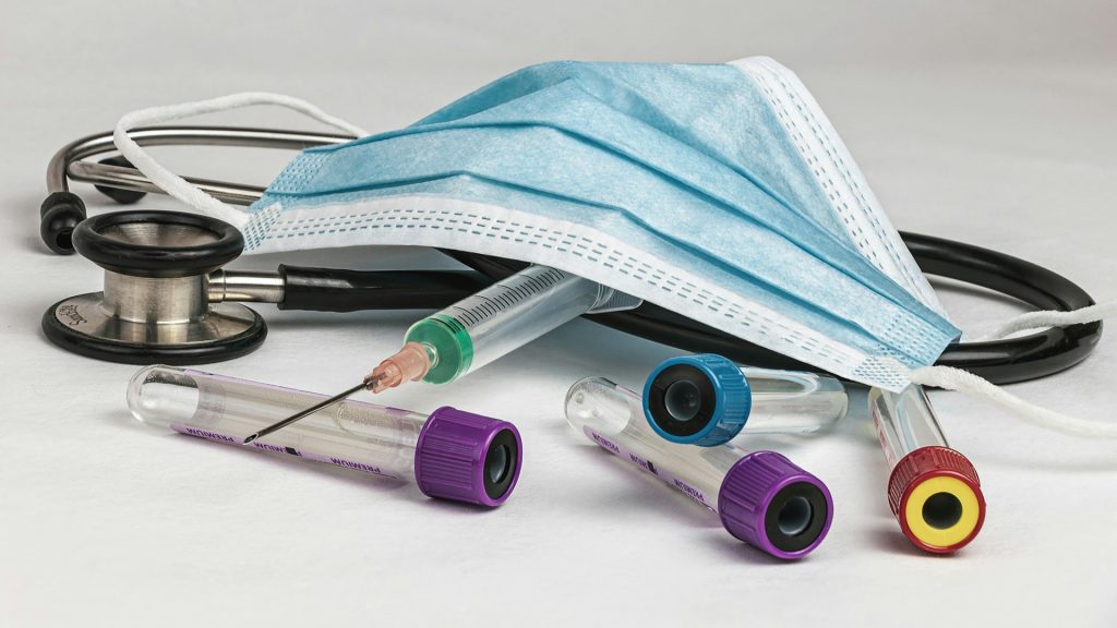 Milieubelasting zorgproducten zichtbaar door mondmasker, stethoscoop, injectienaald en buisjes op witte ondergrond.