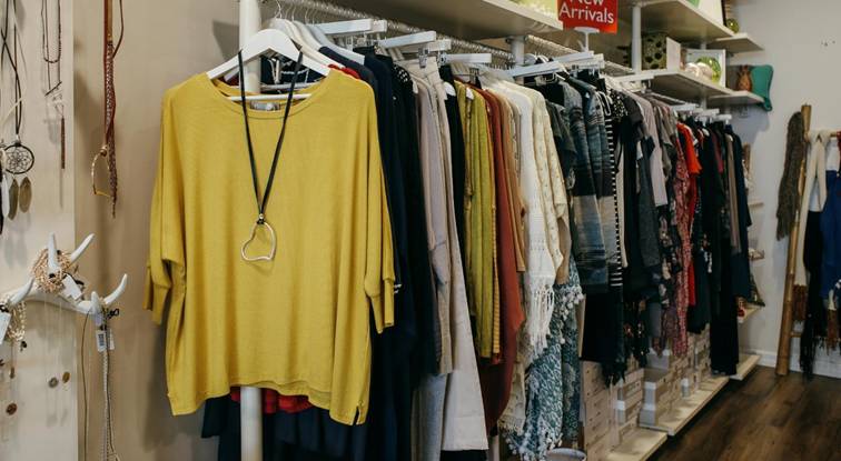 Kledingrekken met kleurrijke damesmode, waaronder een okergele trui met ketting – dameskleding boetiek.