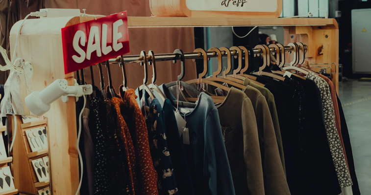 Kledingrek met diverse truien en jurken onder een rood SALE-bord in een winkelruimte